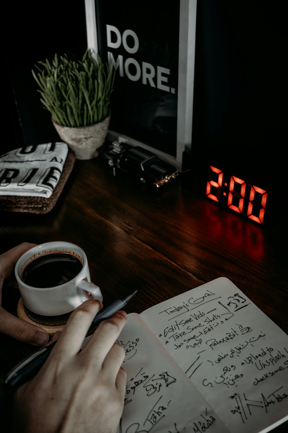 Hands writing in a notebook next to a coffee mug.